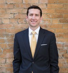 a man wearing a suit and tie standing in front of a brick wall